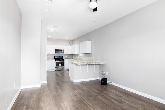 kitchen with kitchen peninsula, a kitchen bar, dark hardwood / wood-style flooring, stainless steel appliances, and white cabinetry