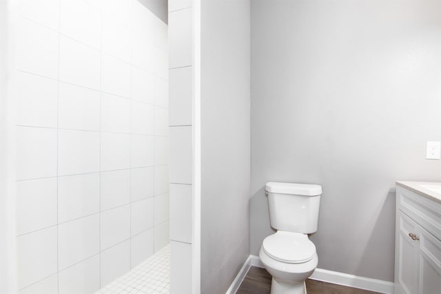 bathroom featuring a tile shower, vanity, wood-type flooring, and toilet