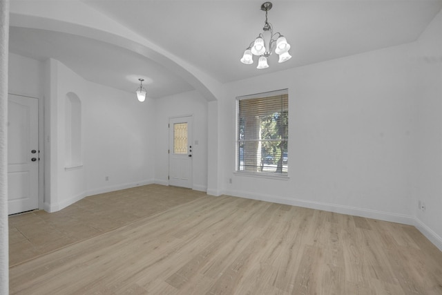 empty room with light hardwood / wood-style floors and an inviting chandelier