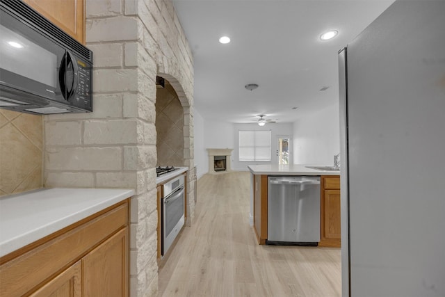 kitchen with sink, light hardwood / wood-style flooring, ceiling fan, a fireplace, and appliances with stainless steel finishes