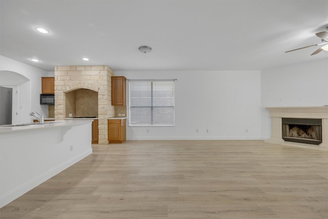 unfurnished living room featuring ceiling fan, a stone fireplace, light wood-type flooring, and sink