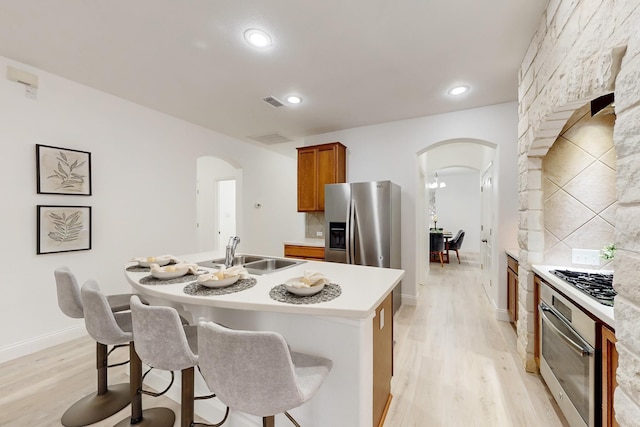 kitchen featuring sink, appliances with stainless steel finishes, a kitchen breakfast bar, an island with sink, and light hardwood / wood-style floors