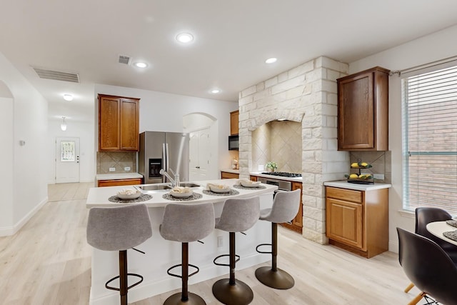 kitchen with sink, stainless steel appliances, tasteful backsplash, a center island with sink, and light wood-type flooring