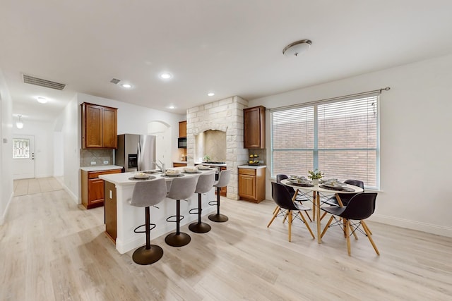 kitchen with stainless steel fridge, a kitchen breakfast bar, tasteful backsplash, light hardwood / wood-style floors, and a kitchen island