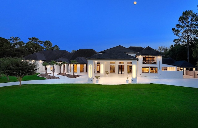 back house at dusk featuring a lawn and a balcony