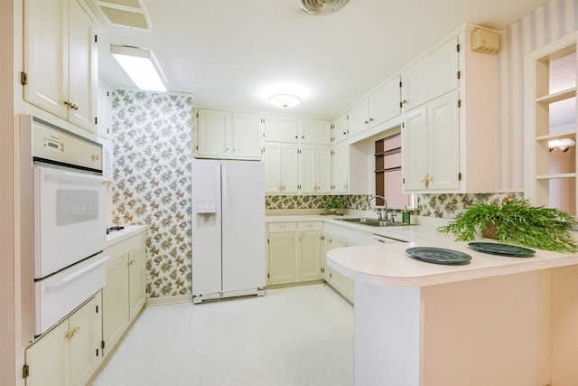 kitchen with white cabinets, sink, white appliances, and kitchen peninsula