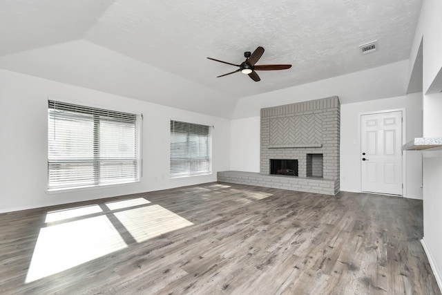 unfurnished living room with lofted ceiling, a brick fireplace, hardwood / wood-style flooring, ceiling fan, and a textured ceiling