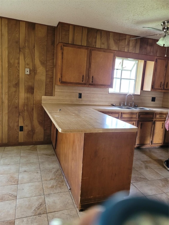 kitchen with kitchen peninsula, a textured ceiling, ceiling fan, sink, and wood walls