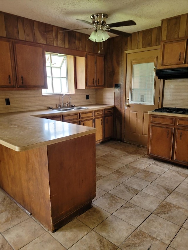 kitchen with extractor fan, wooden walls, tasteful backsplash, kitchen peninsula, and stainless steel gas cooktop