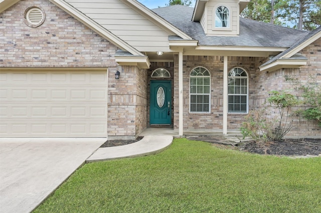 property entrance with brick siding, a shingled roof, a lawn, driveway, and an attached garage