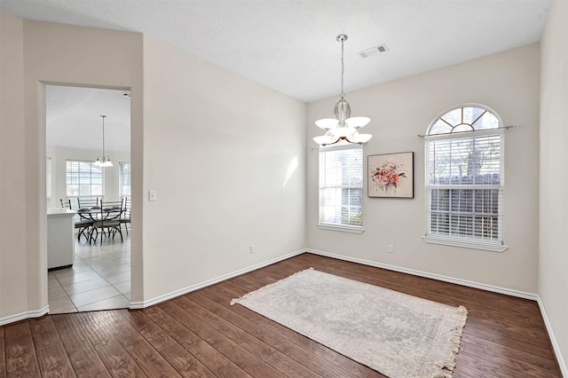 unfurnished dining area with a notable chandelier, wood finished floors, visible vents, and baseboards