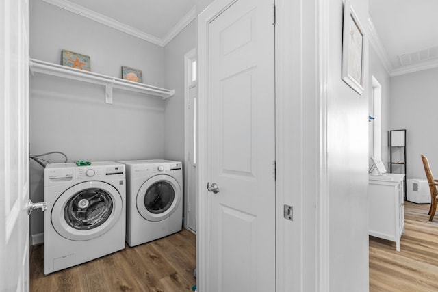 clothes washing area featuring hardwood / wood-style flooring, washing machine and dryer, and ornamental molding