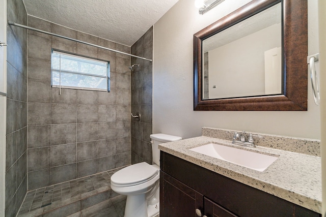 bathroom with a tile shower, vanity, a textured ceiling, and toilet