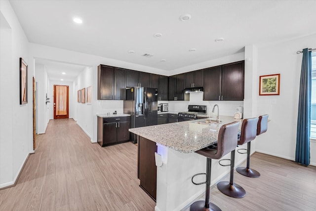 kitchen featuring sink, a kitchen breakfast bar, light wood-type flooring, and black appliances