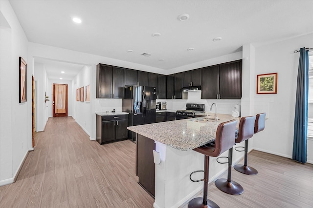 kitchen with light stone countertops, sink, a breakfast bar, black appliances, and light wood-type flooring