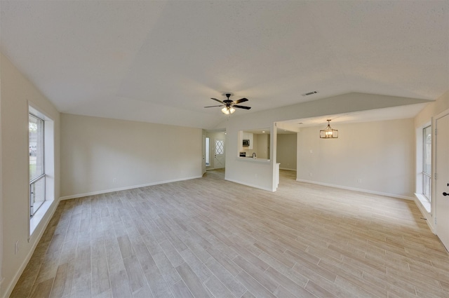 unfurnished living room featuring ceiling fan with notable chandelier, a healthy amount of sunlight, light wood-type flooring, and lofted ceiling