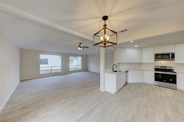 kitchen with sink, hanging light fixtures, appliances with stainless steel finishes, white cabinets, and light wood-type flooring