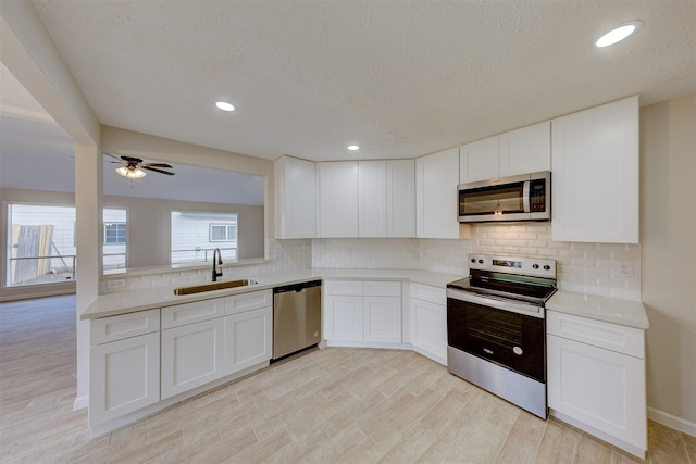 kitchen featuring white cabinetry, sink, tasteful backsplash, light hardwood / wood-style floors, and appliances with stainless steel finishes