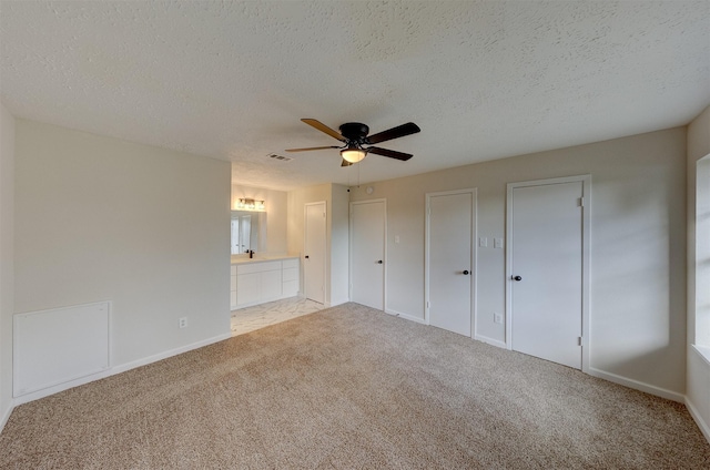 unfurnished bedroom with ensuite bathroom, ceiling fan, a textured ceiling, and two closets