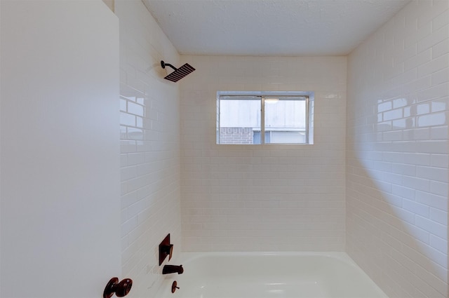 bathroom featuring a textured ceiling and tiled shower / bath