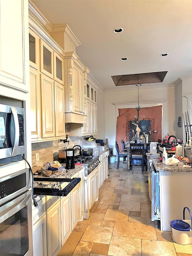 kitchen featuring appliances with stainless steel finishes, dark stone counters, ornamental molding, and pendant lighting