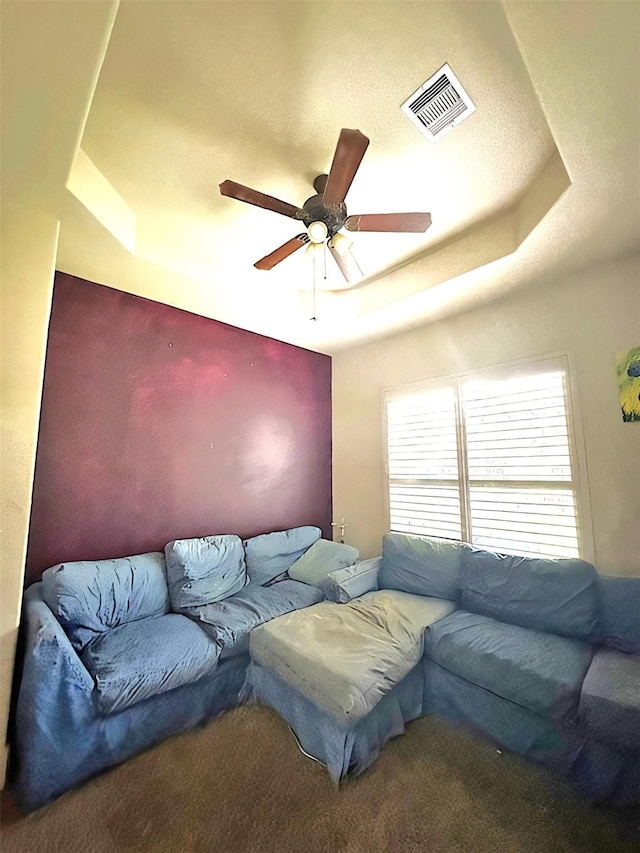 living room with carpet, ceiling fan, and a tray ceiling