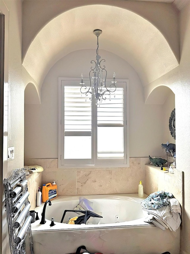 bathroom featuring an inviting chandelier, a bathtub, and lofted ceiling