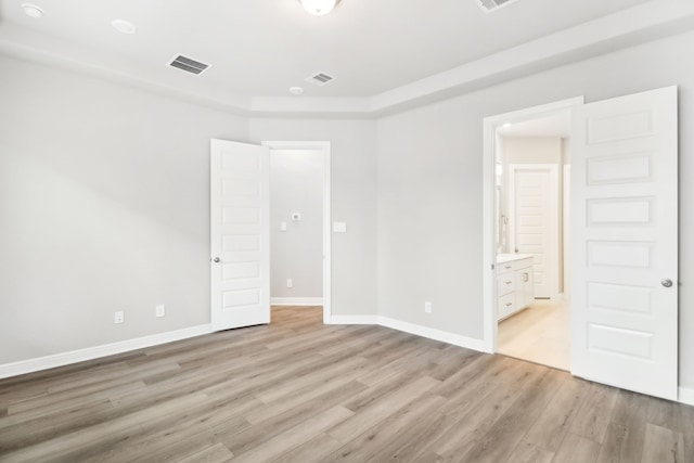 unfurnished bedroom with ensuite bathroom and light wood-type flooring