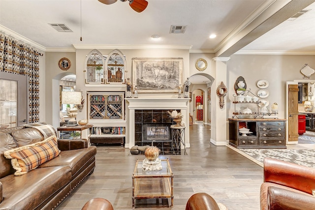 living room with a tiled fireplace, crown molding, and wood-type flooring