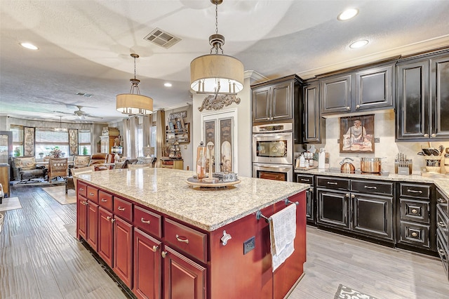 kitchen with a center island, hanging light fixtures, ceiling fan, light wood-type flooring, and stainless steel double oven