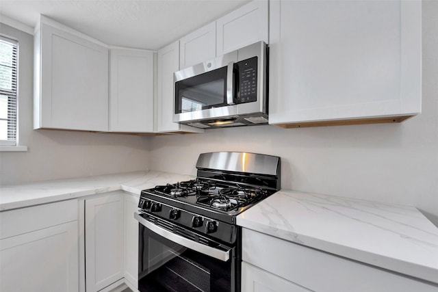 kitchen with light stone countertops, white cabinetry, a textured ceiling, and appliances with stainless steel finishes