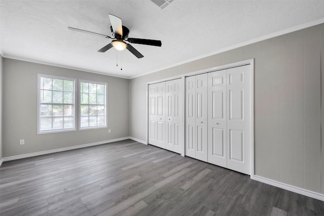 unfurnished bedroom featuring two closets, hardwood / wood-style flooring, ceiling fan, and crown molding