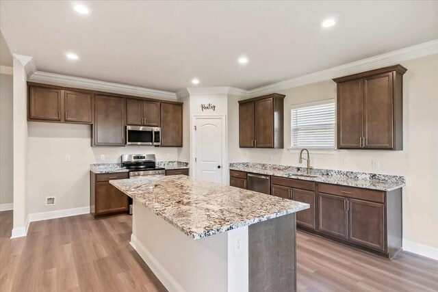 kitchen with sink, a center island, stainless steel appliances, light stone counters, and light wood-type flooring