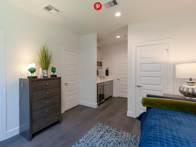 bedroom with ensuite bath, beverage cooler, and dark wood-type flooring