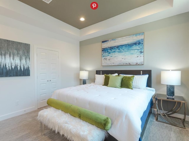 bedroom with light colored carpet, a tray ceiling, and a closet