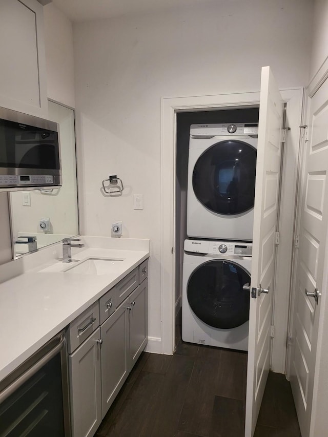 laundry area with sink, dark wood-type flooring, and stacked washer and clothes dryer