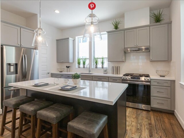 kitchen with decorative backsplash, gray cabinets, a kitchen island, dark hardwood / wood-style flooring, and stainless steel appliances