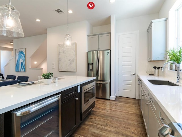 kitchen with appliances with stainless steel finishes, dark hardwood / wood-style flooring, beverage cooler, sink, and hanging light fixtures