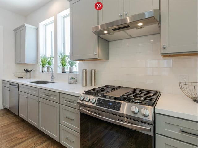 kitchen featuring light wood-type flooring, backsplash, gray cabinetry, stainless steel gas range, and sink