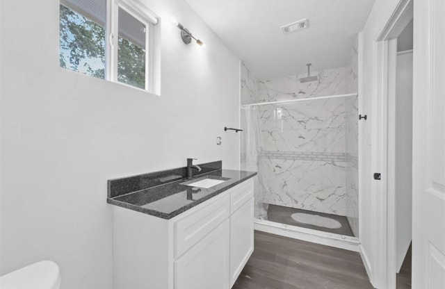 bathroom with toilet, vanity, wood-type flooring, and tiled shower