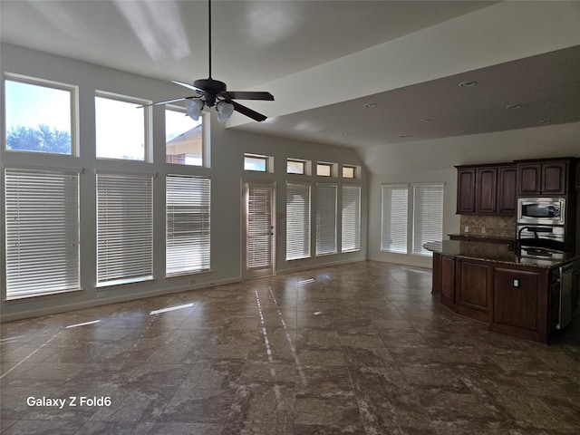 kitchen with decorative backsplash, dark brown cabinets, stainless steel appliances, ceiling fan, and dark stone countertops