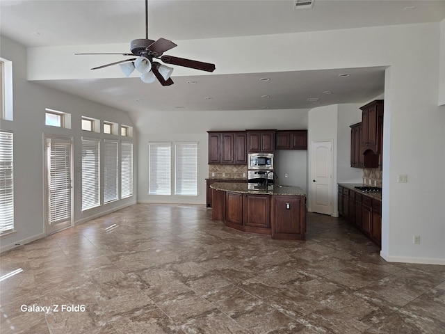 kitchen featuring dark brown cabinetry, ceiling fan, backsplash, a center island with sink, and appliances with stainless steel finishes