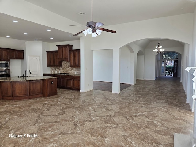 kitchen with ceiling fan with notable chandelier, vaulted ceiling, light stone counters, dark brown cabinetry, and stainless steel appliances