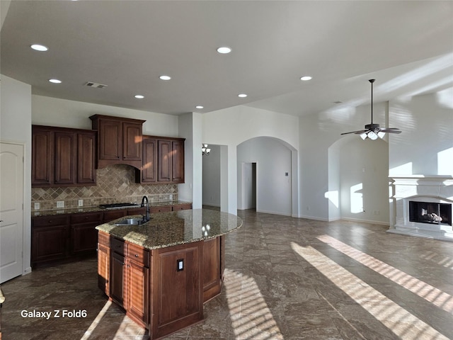 kitchen featuring dark brown cabinets, ceiling fan, a kitchen island with sink, sink, and stone countertops