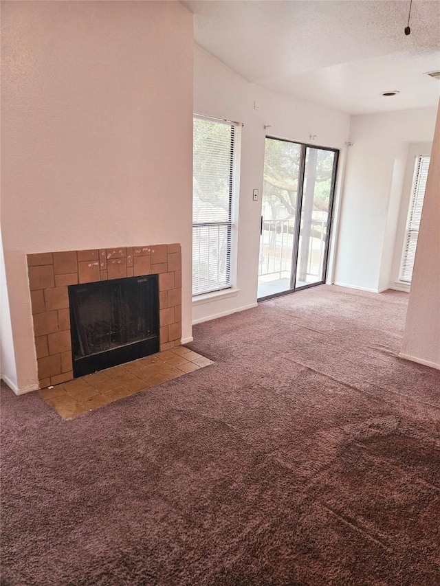 unfurnished living room featuring a textured ceiling, a fireplace, carpet floors, and plenty of natural light