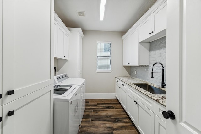 laundry room featuring washing machine and clothes dryer, dark hardwood / wood-style flooring, sink, and cabinets