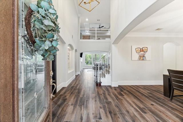 foyer featuring a chandelier, ornamental molding, a towering ceiling, and dark wood-type flooring