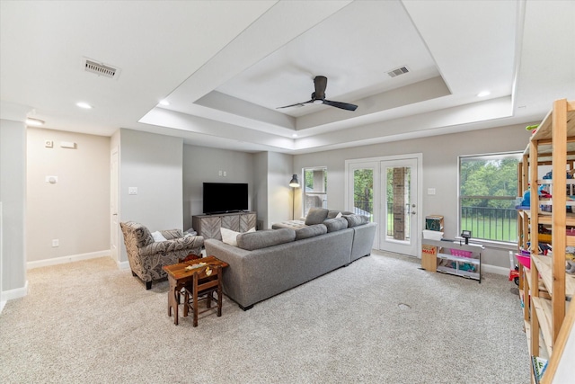 living room with a tray ceiling, light carpet, and ceiling fan