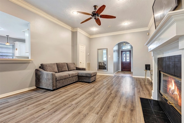 living room featuring ornamental molding, a textured ceiling, ceiling fan, light hardwood / wood-style flooring, and a tiled fireplace