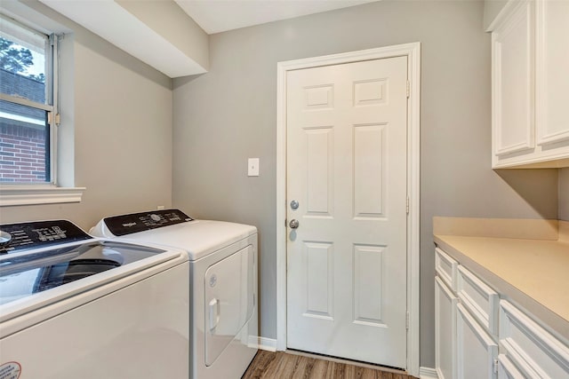 clothes washing area with washing machine and dryer, hardwood / wood-style floors, and cabinets